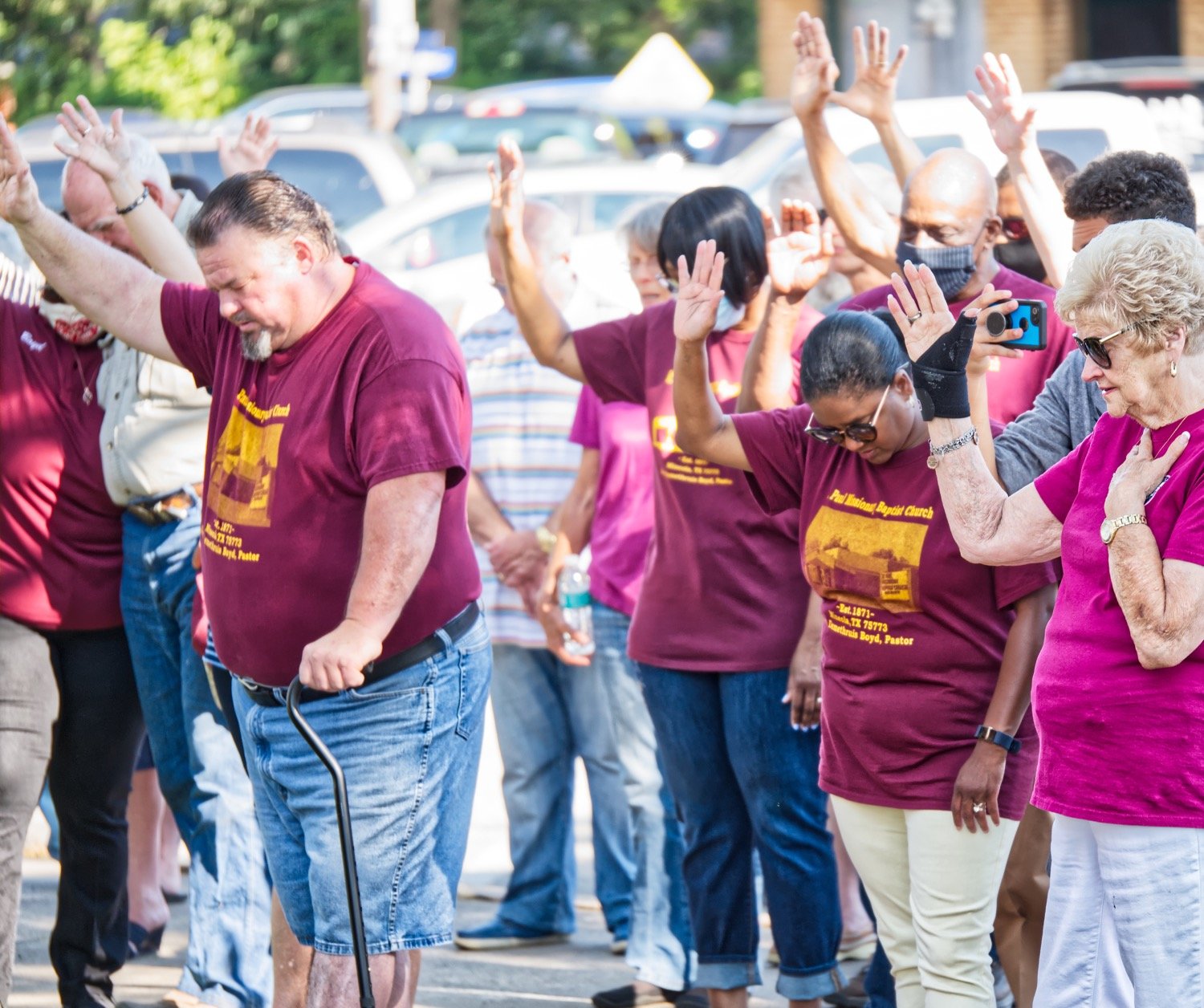 Participants at the Saturday morning prayer service on the courthouse square in Quitman raise hands in unison.